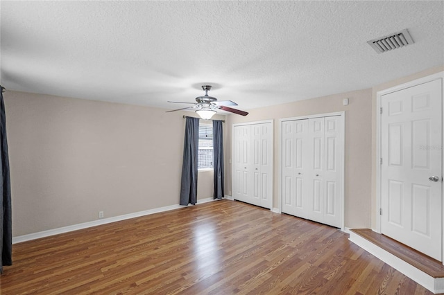 unfurnished bedroom featuring baseboards, visible vents, wood finished floors, a textured ceiling, and multiple closets