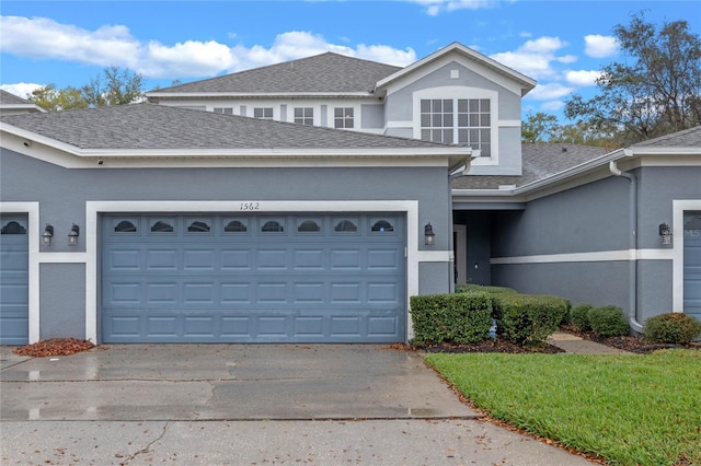 traditional-style house with a garage, concrete driveway, a shingled roof, and stucco siding