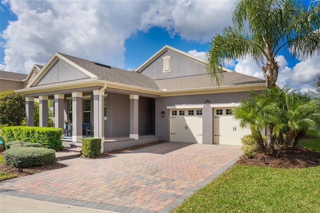 view of front of house featuring covered porch, decorative driveway, a garage, and stucco siding