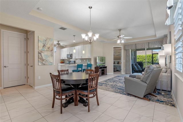 dining space with ceiling fan with notable chandelier, a tray ceiling, visible vents, and baseboards