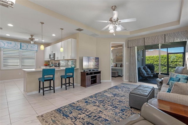 living area with recessed lighting, visible vents, baseboards, a ceiling fan, and a raised ceiling