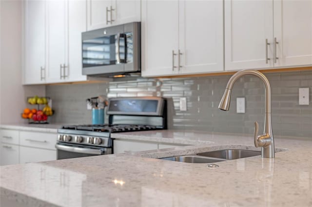 kitchen featuring white cabinets, decorative backsplash, light stone counters, stainless steel appliances, and a sink