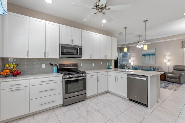 kitchen featuring appliances with stainless steel finishes, open floor plan, white cabinetry, a sink, and a peninsula