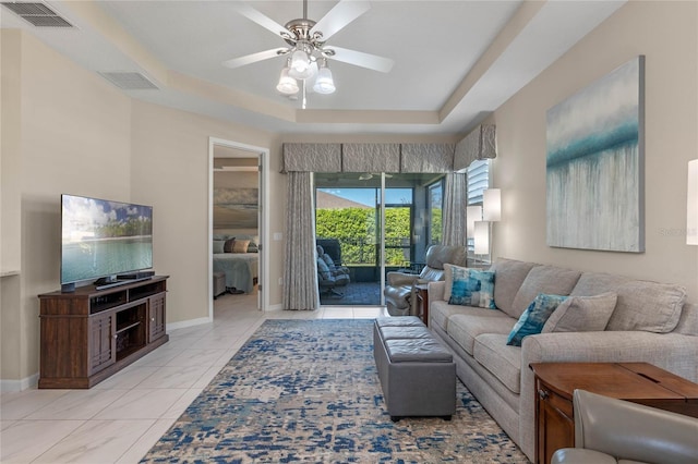 living area with ceiling fan, visible vents, a raised ceiling, and baseboards