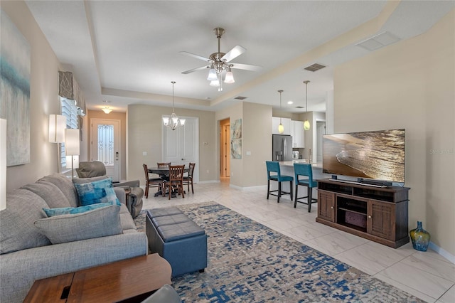 living room featuring baseboards, visible vents, a tray ceiling, and ceiling fan with notable chandelier