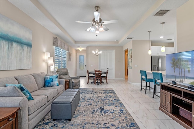 living area featuring ceiling fan with notable chandelier, visible vents, baseboards, marble finish floor, and a raised ceiling