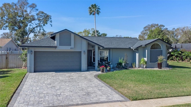 view of front of property with an attached garage, fence, decorative driveway, stucco siding, and a front lawn