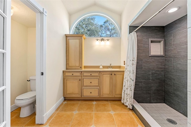 bathroom featuring lofted ceiling, toilet, a tile shower, tile patterned flooring, and baseboards