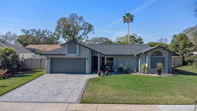 view of front facade featuring an attached garage, fence, decorative driveway, stucco siding, and a front lawn