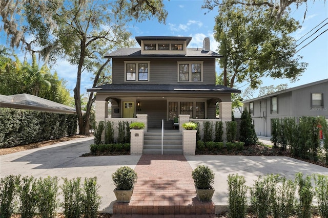 american foursquare style home with covered porch, concrete driveway, brick siding, and a chimney