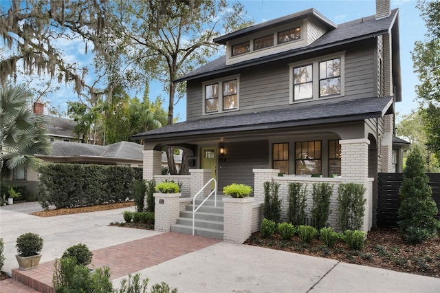 american foursquare style home with covered porch, brick siding, and a chimney