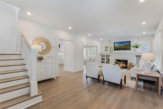 living room featuring stairs, a brick fireplace, wood finished floors, and recessed lighting