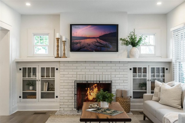 living area with a fireplace, wood finished floors, visible vents, and a healthy amount of sunlight