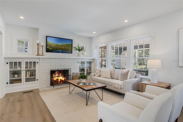 living area with recessed lighting, a brick fireplace, visible vents, and wood finished floors