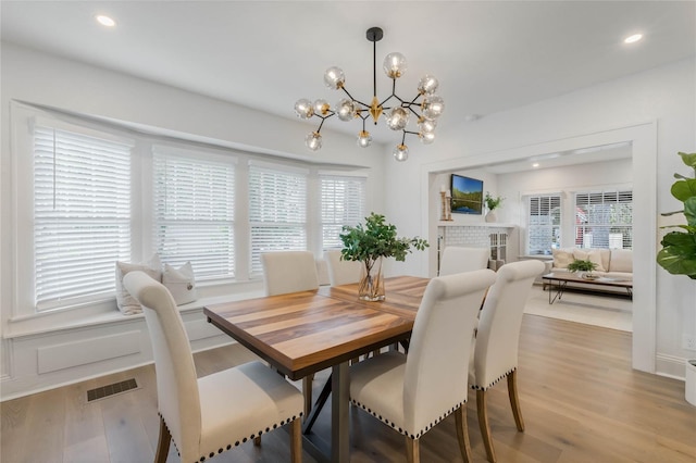 dining room with visible vents, light wood-style flooring, a fireplace, a notable chandelier, and recessed lighting