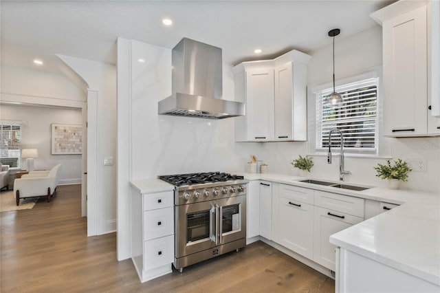 kitchen featuring a healthy amount of sunlight, wall chimney range hood, range with two ovens, and a sink