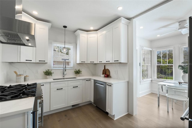 kitchen with appliances with stainless steel finishes, wood finished floors, a sink, wall chimney range hood, and backsplash