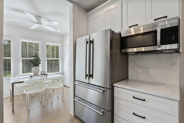 kitchen featuring light stone counters, stainless steel appliances, light wood-style flooring, a ceiling fan, and white cabinetry