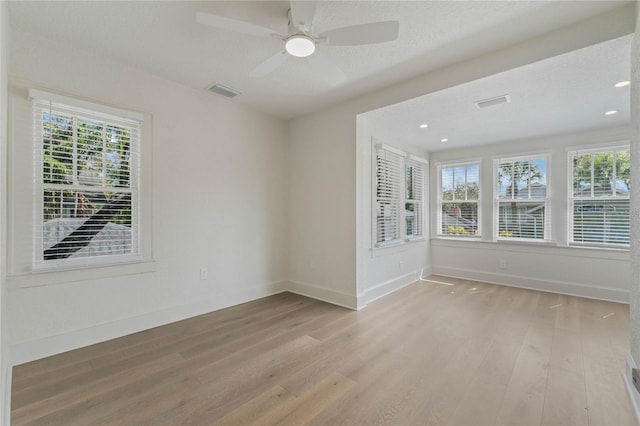 unfurnished room featuring light wood-style flooring, a textured ceiling, visible vents, and baseboards