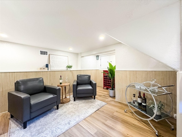 living area with wooden walls, wainscoting, visible vents, and wood finished floors