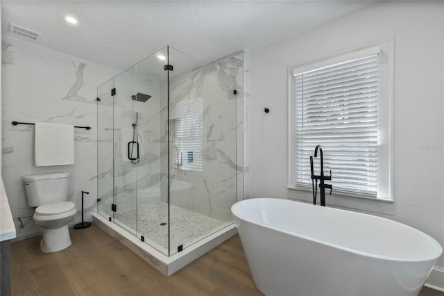 bathroom featuring a marble finish shower, visible vents, toilet, wood finished floors, and a freestanding tub