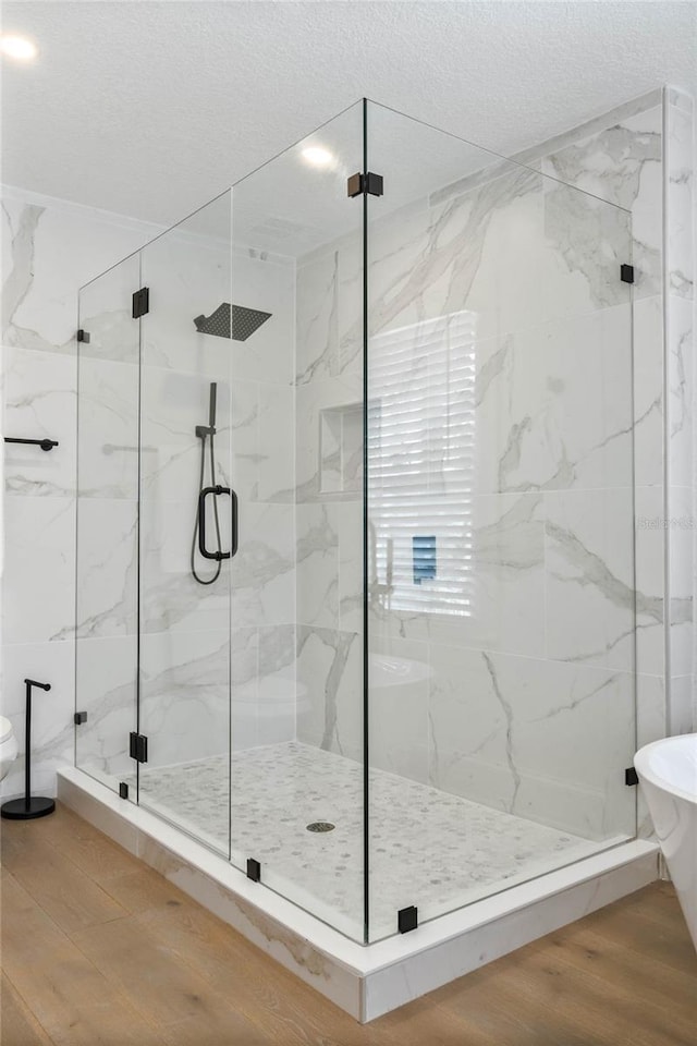 bathroom with a freestanding tub, a textured ceiling, a marble finish shower, and wood finished floors