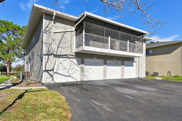 back of property featuring a garage, a sunroom, central AC unit, and aphalt driveway