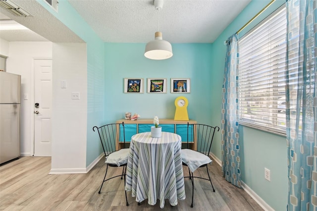 dining area with light wood-type flooring, visible vents, a textured ceiling, and baseboards