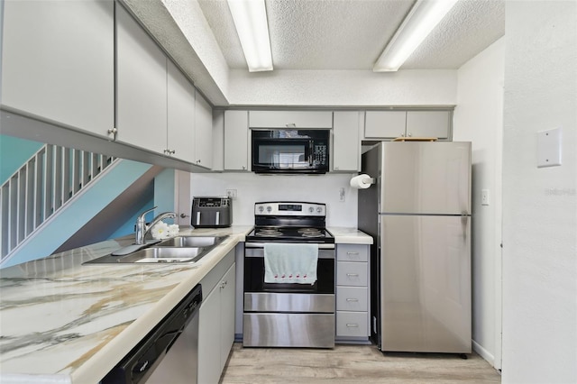 kitchen with stainless steel appliances, a textured ceiling, light countertops, light wood-type flooring, and a sink