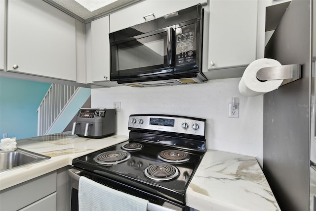 kitchen featuring black microwave, light countertops, white cabinets, and stainless steel range with electric cooktop