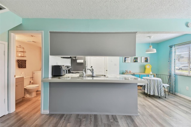 kitchen with light wood-style floors, a sink, a peninsula, and a textured ceiling