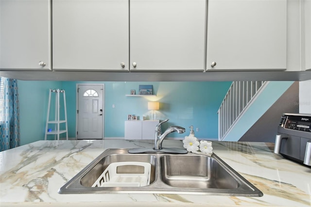 kitchen featuring white cabinetry, a sink, and light stone countertops