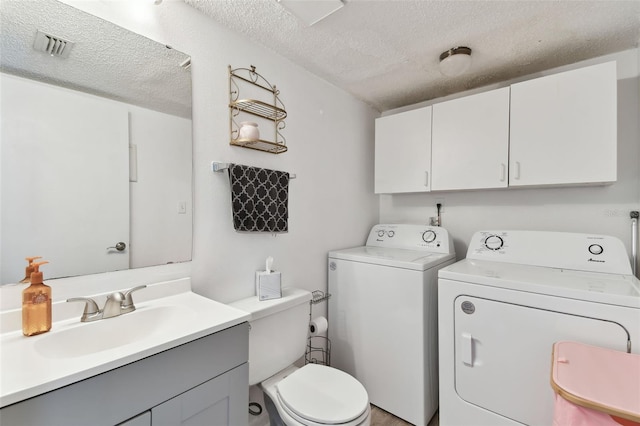 bathroom with a textured ceiling, toilet, visible vents, vanity, and independent washer and dryer