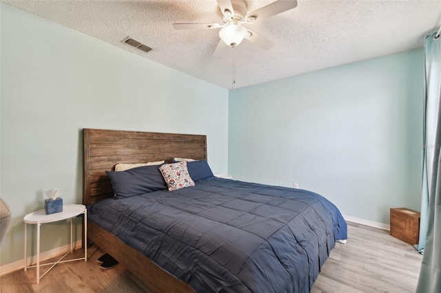 bedroom featuring baseboards, visible vents, a ceiling fan, wood finished floors, and a textured ceiling