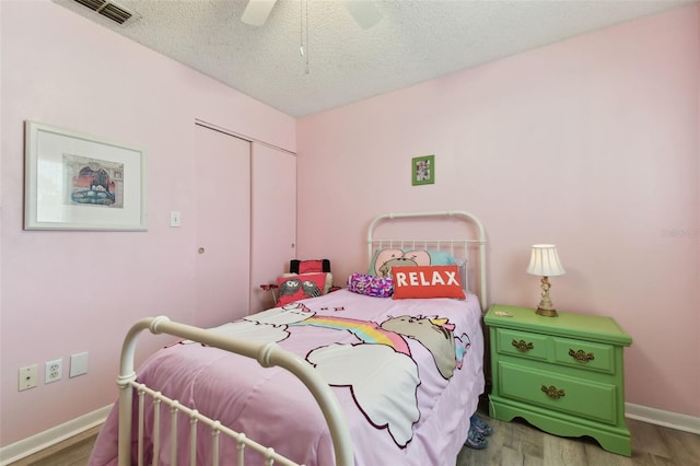 bedroom featuring a closet, visible vents, a textured ceiling, wood finished floors, and baseboards