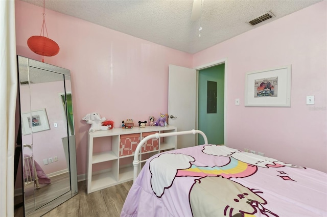 bedroom featuring electric panel, visible vents, a textured ceiling, and wood finished floors