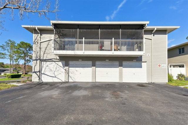 rear view of property featuring aphalt driveway, an attached garage, and a balcony