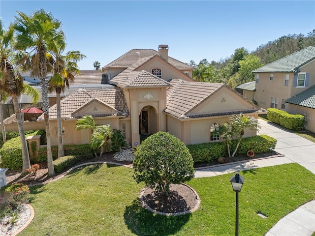 mediterranean / spanish home with a tile roof, a chimney, a front yard, and stucco siding