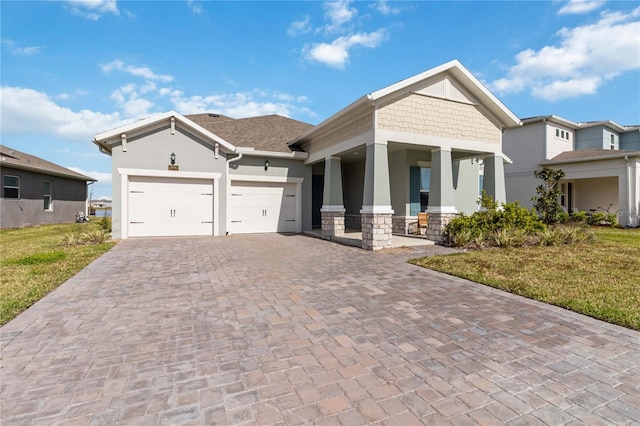 craftsman house with an attached garage, covered porch, stucco siding, a front lawn, and decorative driveway