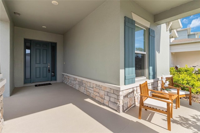 entrance to property featuring stone siding, covered porch, and stucco siding