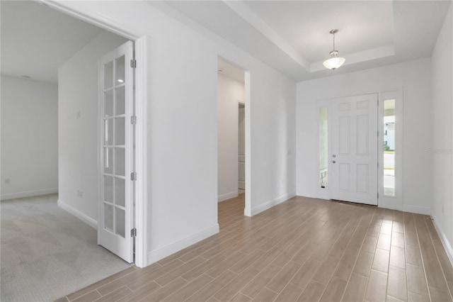 foyer featuring baseboards, a tray ceiling, and wood finished floors