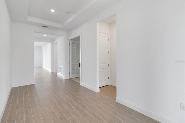 spare room featuring a tray ceiling, visible vents, light wood-type flooring, and baseboards