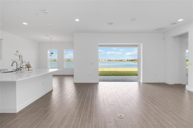 unfurnished living room with visible vents, baseboards, a water view, recessed lighting, and wood finished floors