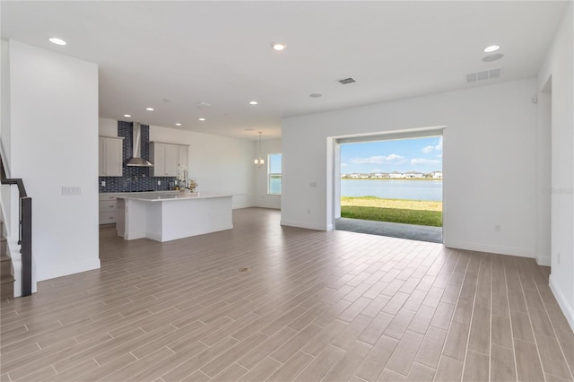 unfurnished living room featuring visible vents, a water view, recessed lighting, light wood finished floors, and stairs