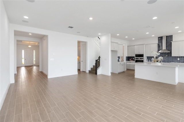 kitchen featuring visible vents, light countertops, wall chimney range hood, tasteful backsplash, and open floor plan