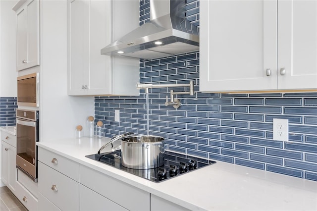 kitchen with white cabinets, wall chimney exhaust hood, tasteful backsplash, and appliances with stainless steel finishes