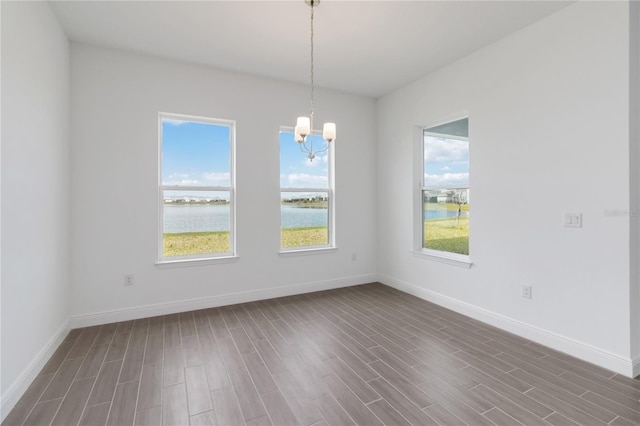 unfurnished room with dark wood-style flooring, a healthy amount of sunlight, an inviting chandelier, and a water view