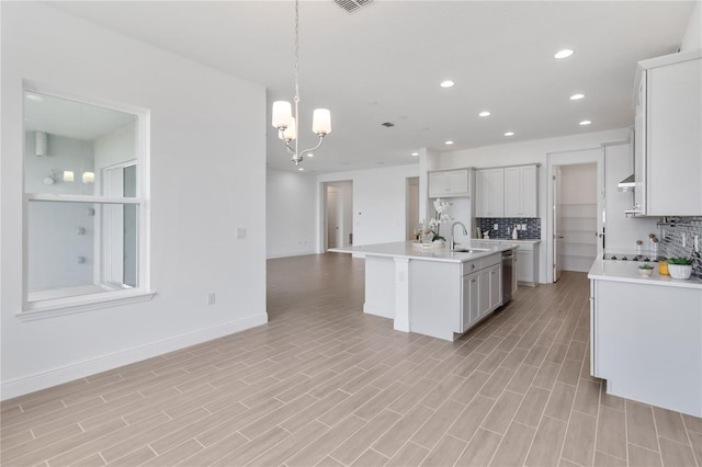 kitchen with a sink, backsplash, stainless steel dishwasher, open floor plan, and light countertops