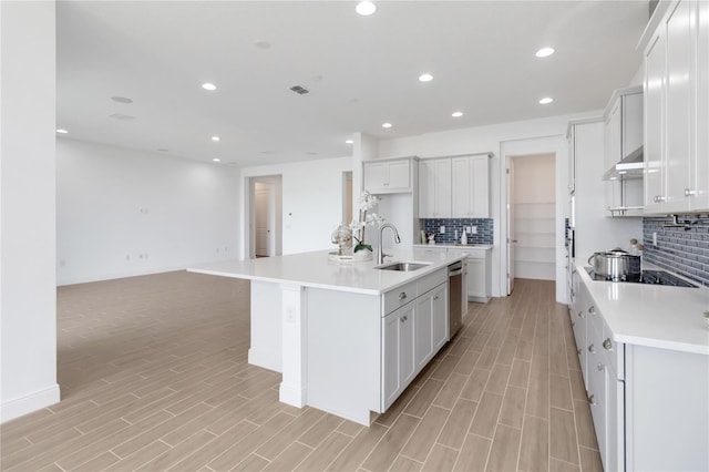 kitchen with a sink, under cabinet range hood, stainless steel dishwasher, open floor plan, and light countertops