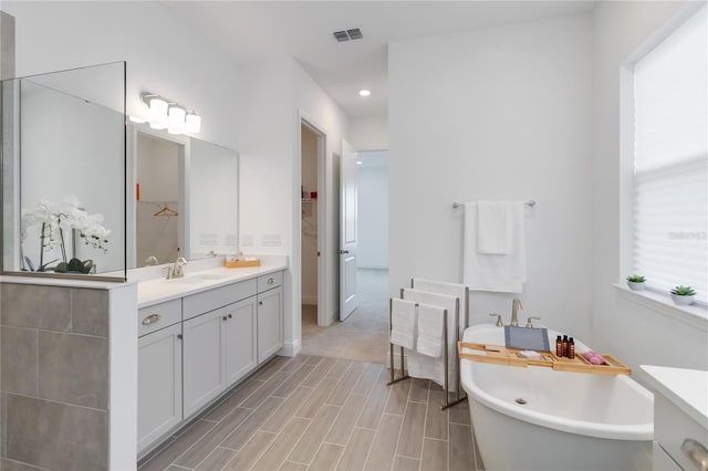 bathroom featuring vanity, wood finished floors, visible vents, a soaking tub, and a walk in closet